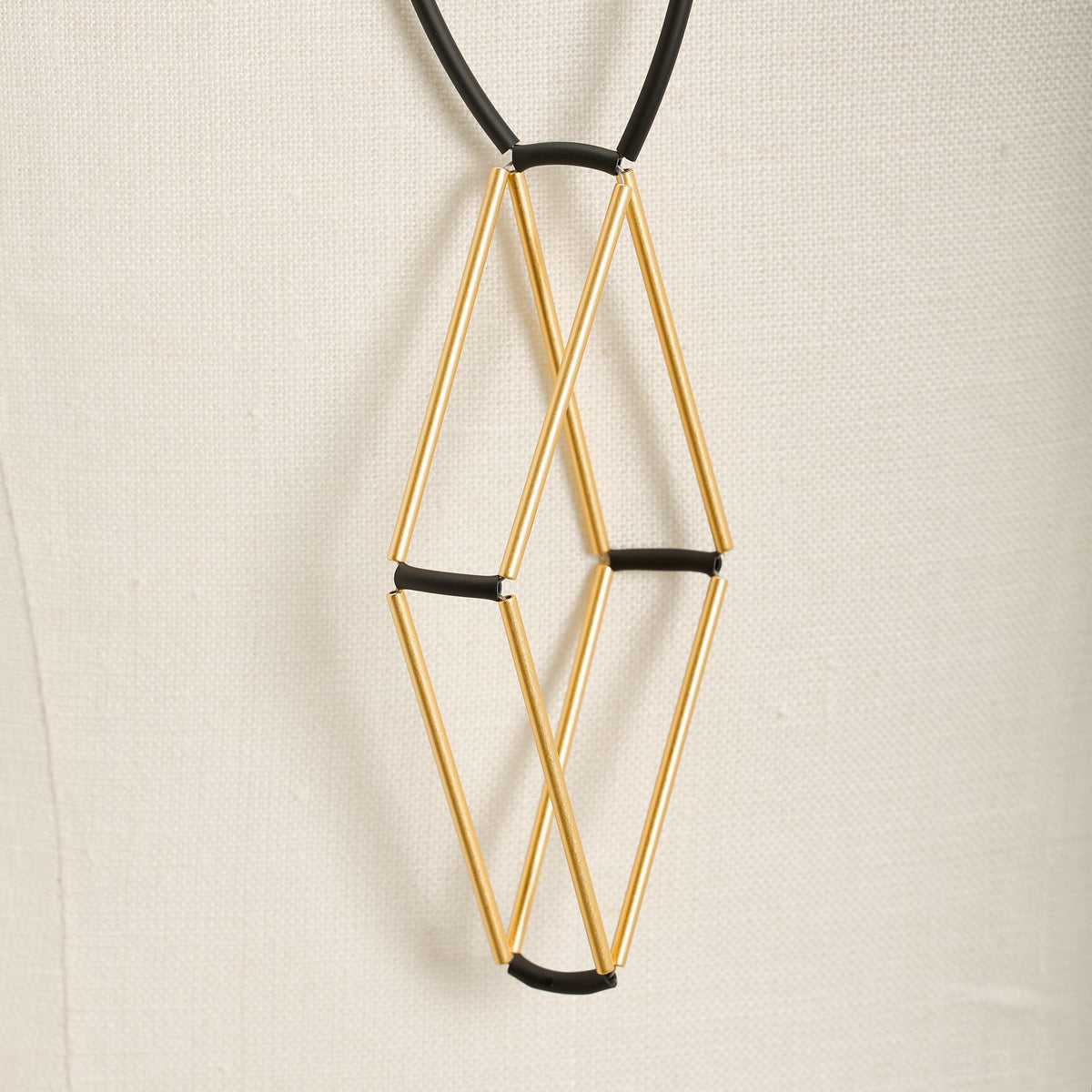 Collana Teorema Oro in ottone dorato e caucciù, variante nero, dettaglio ravvicinato su fondo chiaro