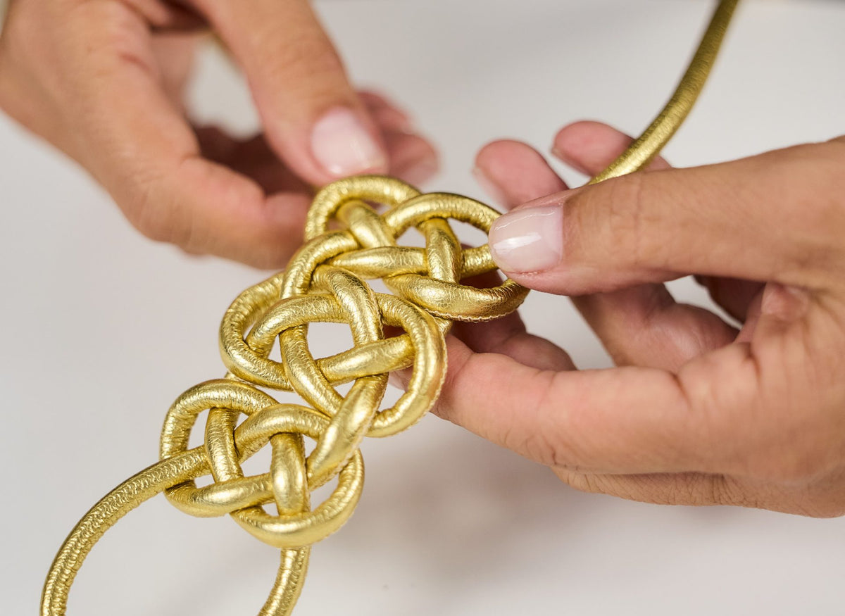 Hands tightening a knot in gold cord